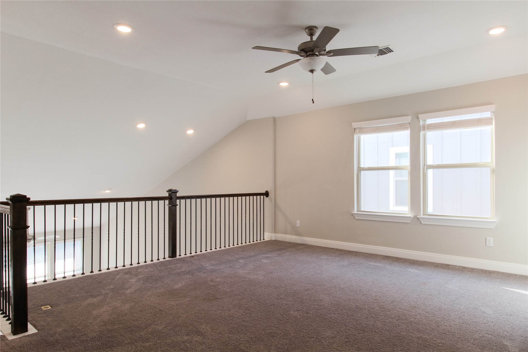 109 Yellow Thistle Cove Georgetown, TX 78626 - Photo 20 of 36 Carpeted loft featuring a vaulted ceiling with recessed lighting, two windows with roller shades, a ceiling fan, and a dark wood and metal baluster railing