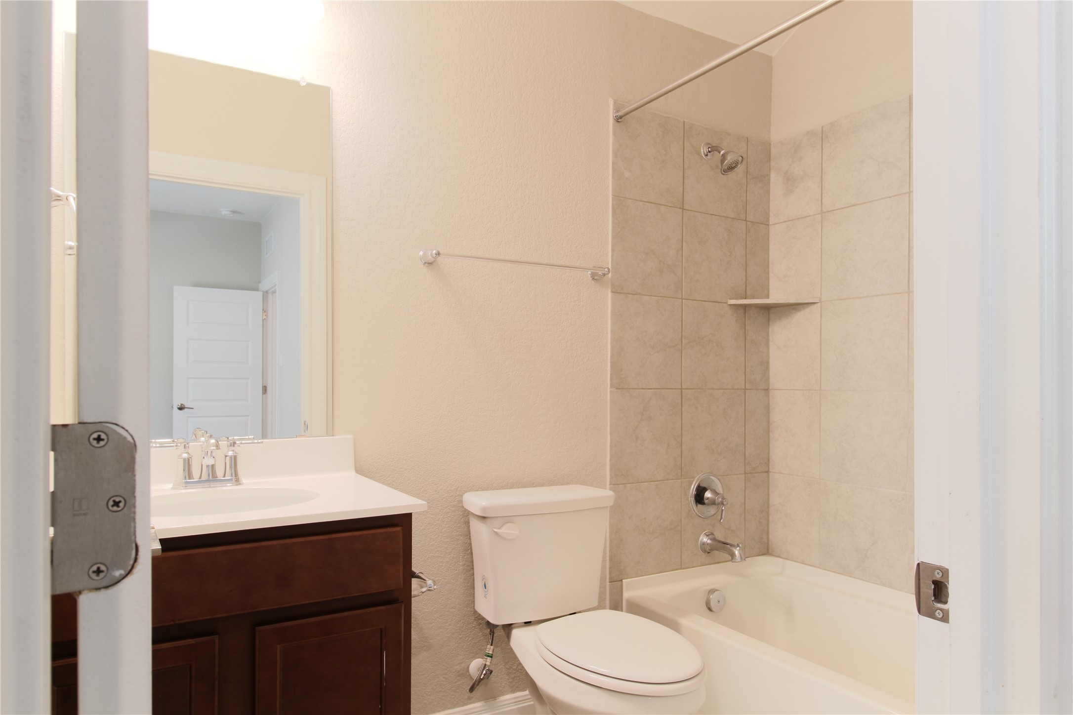 109 Yellow Thistle Cove Georgetown, TX 78626 - Photo 24 of 36 Contemporary bathroom featuring a dark wood-finish vanity with a white countertop and undermount sink, a toilet, and a bathtub with light-colored tile surround and a built-in shelf