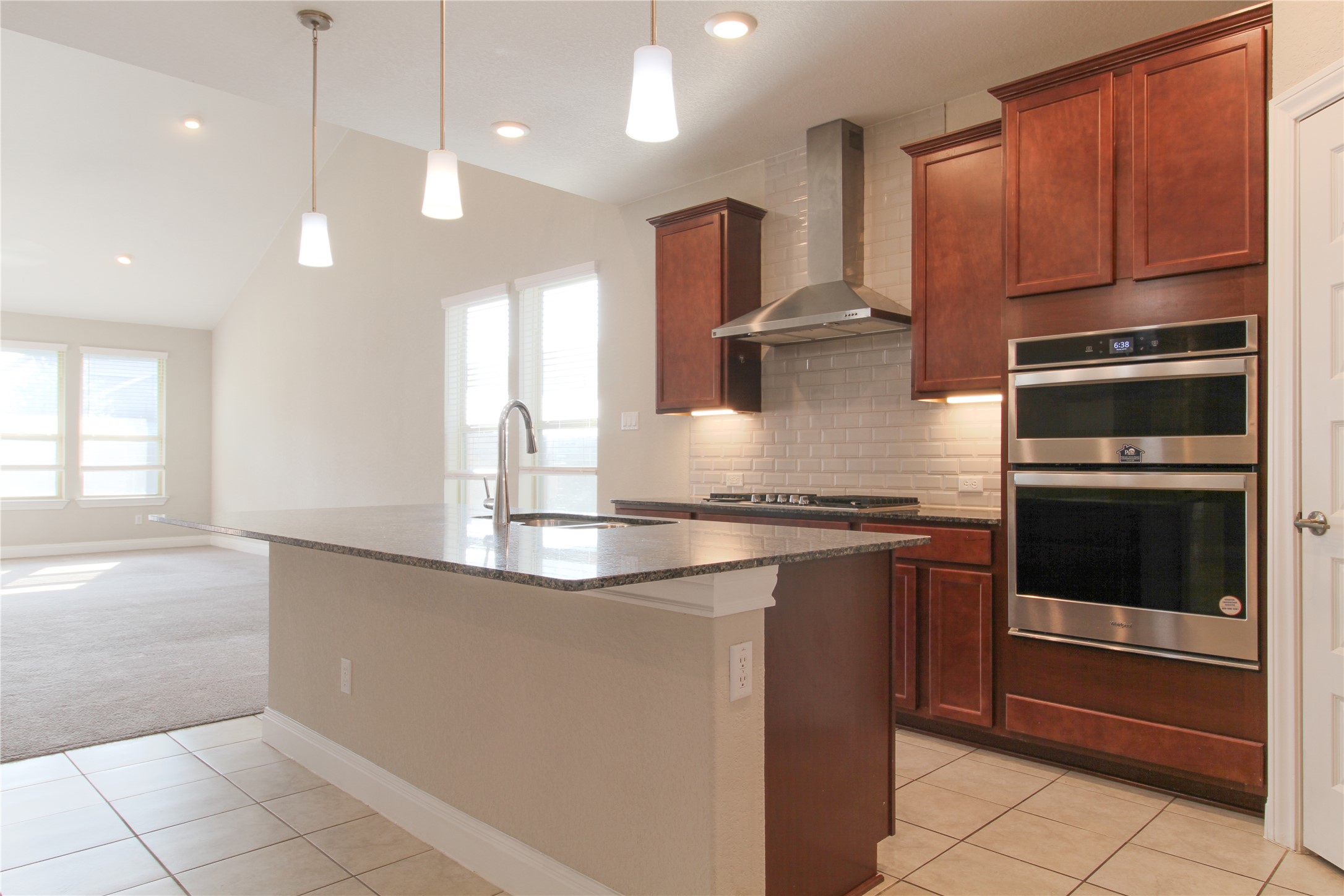 109 Yellow Thistle Cove Georgetown, TX 78626 - Photo 4 of 36 Kitchen featuring a central island with a granite countertop and integrated sink, pendant lighting, warm wood cabinetry, stainless steel double wall ovens, and a tile backsplash