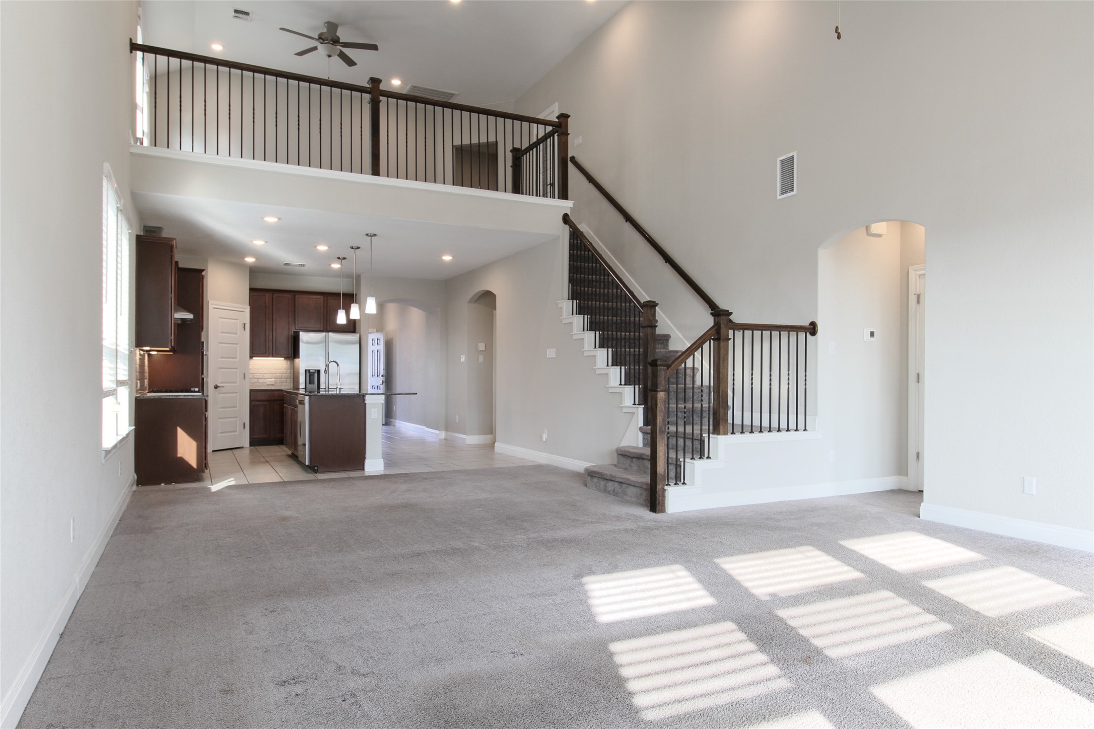 109 Yellow Thistle Cove Georgetown, TX 78626 - Photo 7 of 36 Open-concept living area featuring a two-story ceiling, carpeted flooring, and a staircase with dark wood handrails and black iron balusters
