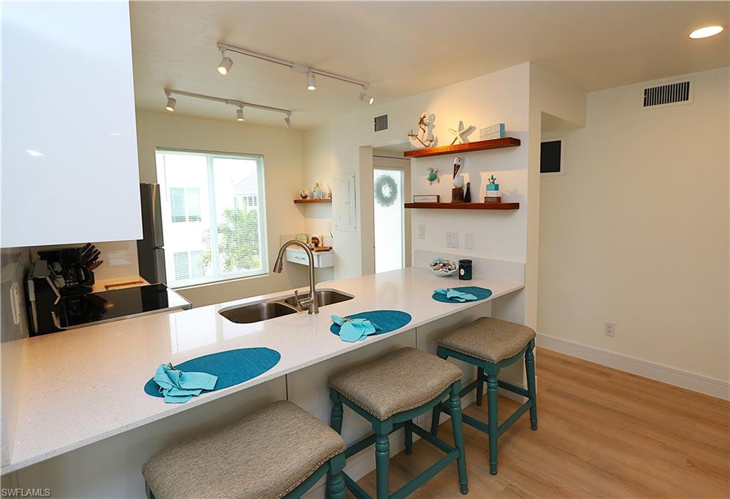 2235 San Marco Road, Unit 5204 Marco Island, FL 34145 - Photo 11 of 42 Kitchen featuring a kitchen breakfast bar, a peninsula, light wood-style floors, open shelves, and light stone counters