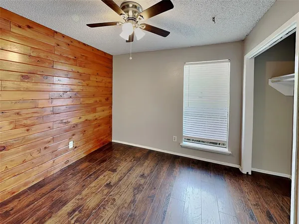 an empty room with wooden floor chandelier fan and windows