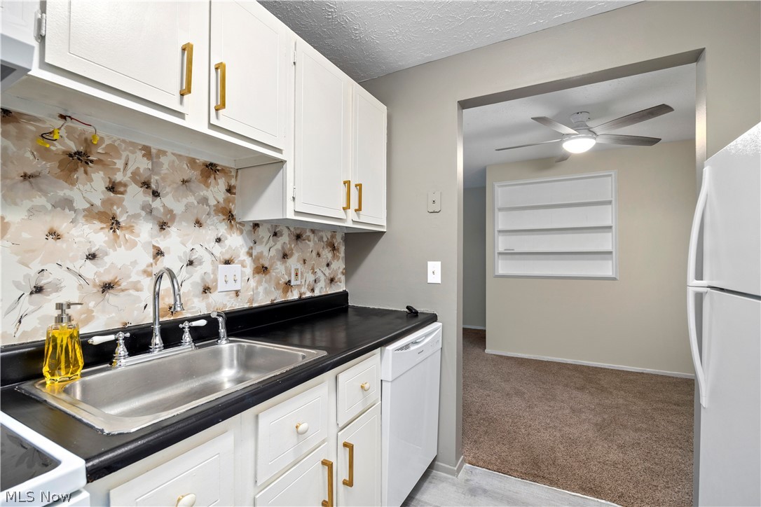 216 Moore Road Avon Lake, OH 44012 - Photo 11 of 22 White cabinetry with gold-tone hardware, stainless steel sink with chrome faucet, floral-patterned backsplash, and dark countertops
