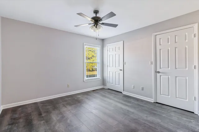 an empty room with wooden floor chandelier fan and windows