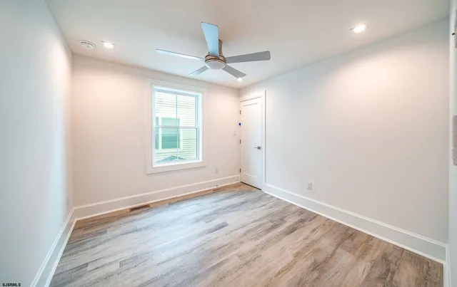 an empty room with wooden floor ceiling fan and windows
