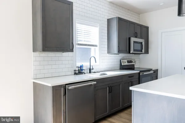 a living room with stainless steel appliances kitchen island granite countertop a refrigerator a stove a sink dishwasher with wooden floor and cabinets