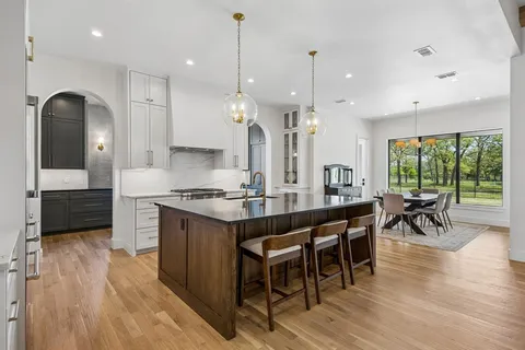 a kitchen with stainless steel appliances granite countertop a stove a sink a oven a dining table and chairs with wooden floor