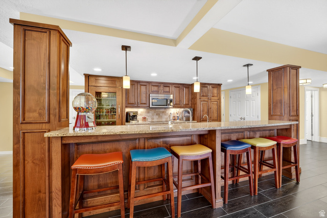714 Draper Heights Way Draper, UT 84020 - Photo 50 of 88 Kitchen with wood finish cabinetry, a breakfast bar area, a peninsula, light stone counters, and pendant lighting