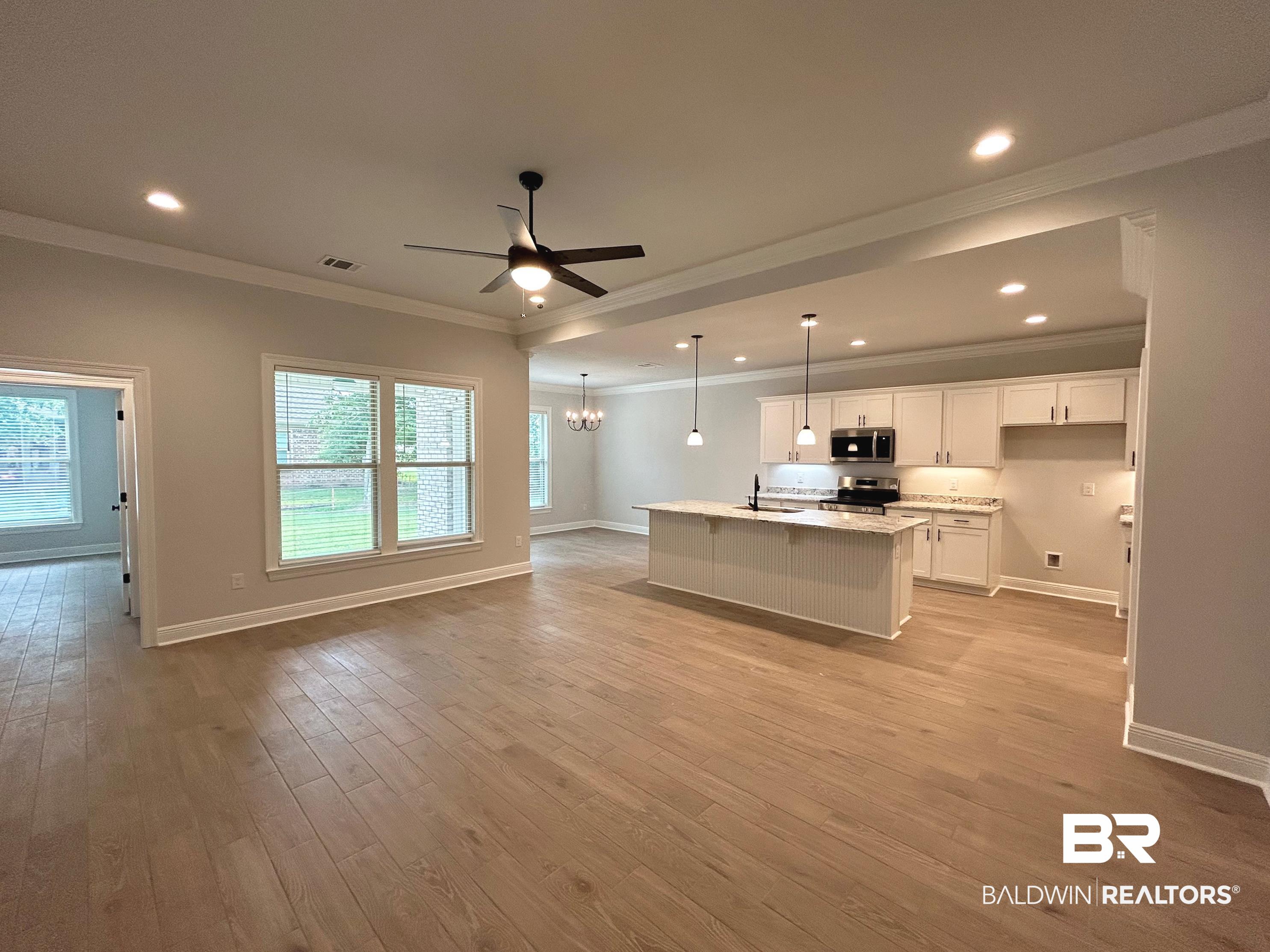 860 Sumter Loop Foley, AL 36535 - Photo 4 of 26 Unfurnished living room featuring ceiling fan with notable chandelier, light wood-type flooring, crown molding, and a wealth of natural light