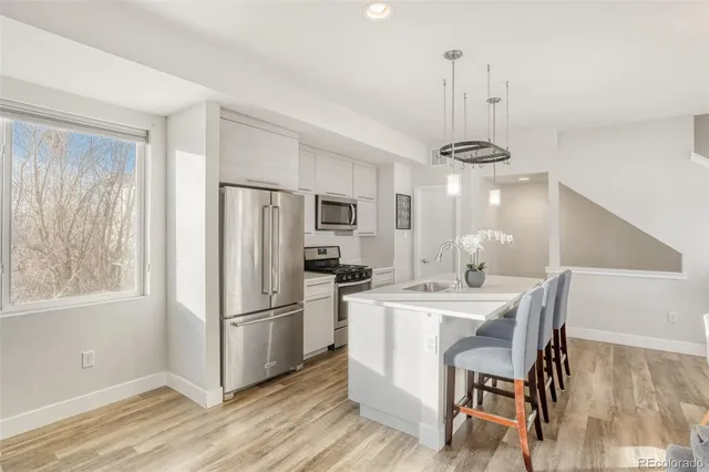 a kitchen with kitchen island a refrigerator a stove a sink dishwasher a dining table and chairs with wooden floor