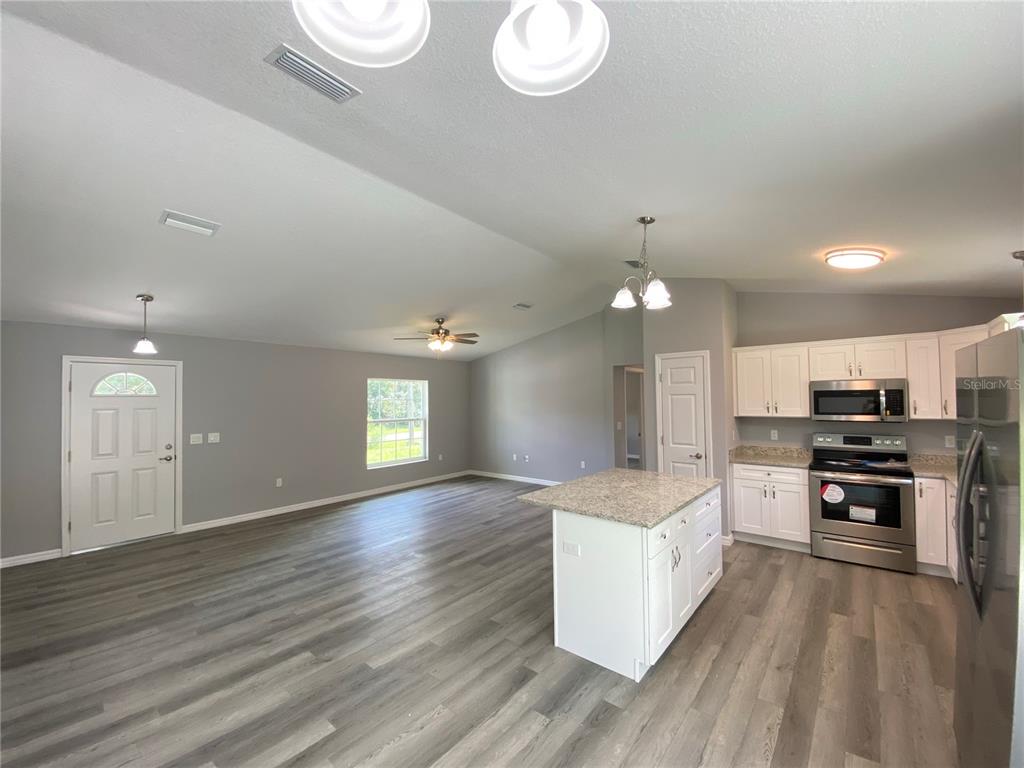 2458 Southwest 170th Loop Ocala, FL 34473 - Photo 9 of 25 a large white kitchen with kitchen island a stove a refrigerator a oven a dining table and chairs with wooden floor