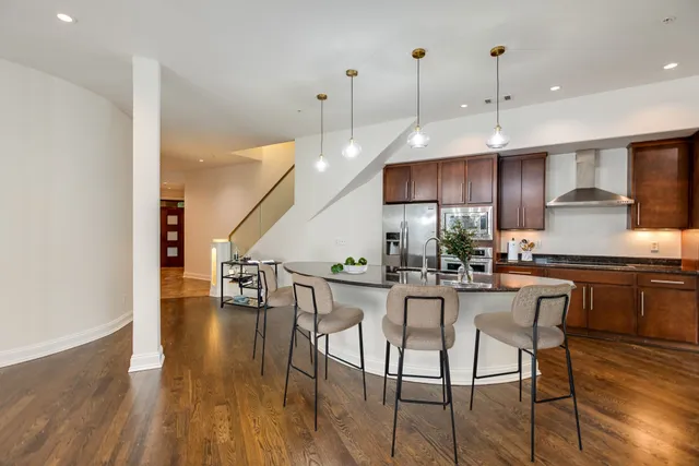 a kitchen with stainless steel appliances granite countertop a stove top oven a sink a dining table and chairs with wooden floor