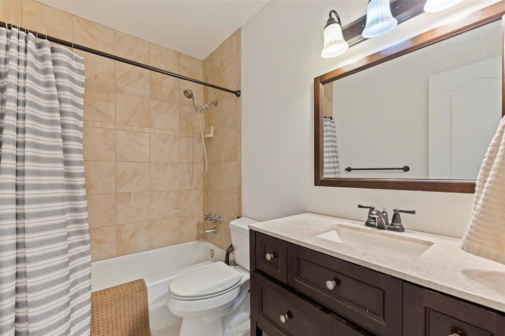 8911 Blind Pass Road, Unit 319 St. Pete Beach, FL 33706 - Photo 23 of 29 a bathroom with a granite countertop sink a toilet and a mirror