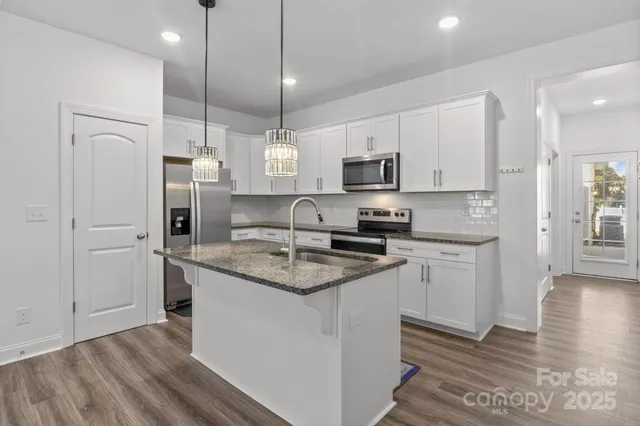 a kitchen with stainless steel appliances granite countertop a sink a stove a refrigerator and white cabinets with wooden floor