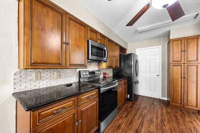 a kitchen with granite countertop stainless steel appliances a sink stove top oven and wooden floor