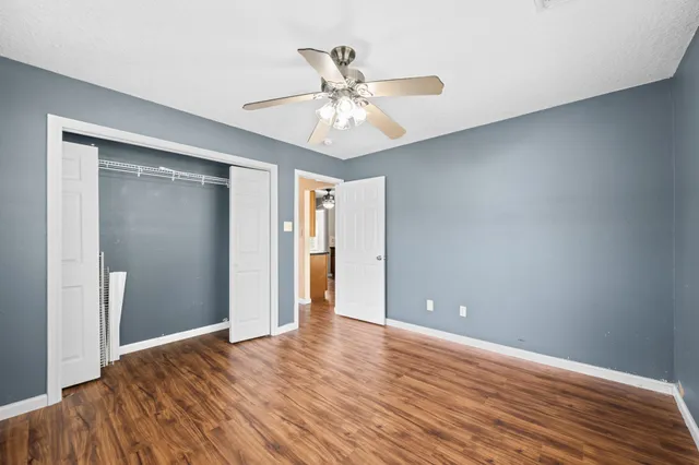 a view of an empty room with wooden floor and a ceiling fan