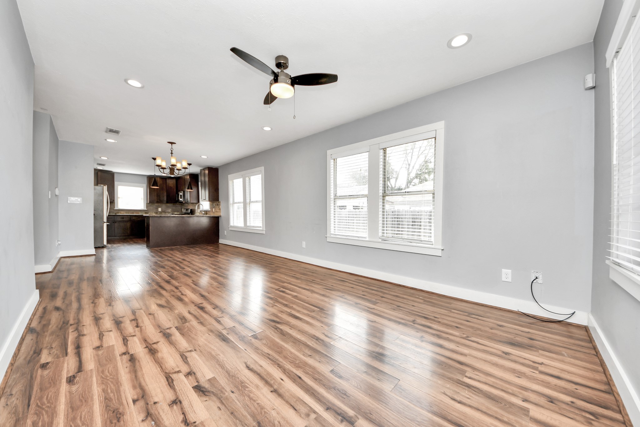2820 Holman Street Houston, TX 77004 - Photo 11 of 38 This spacious, open-plan living area features elegant wood laminate flooring, ample natural light from large windows, and a modern kitchen with dark cabinetry and stainless steel appliances.