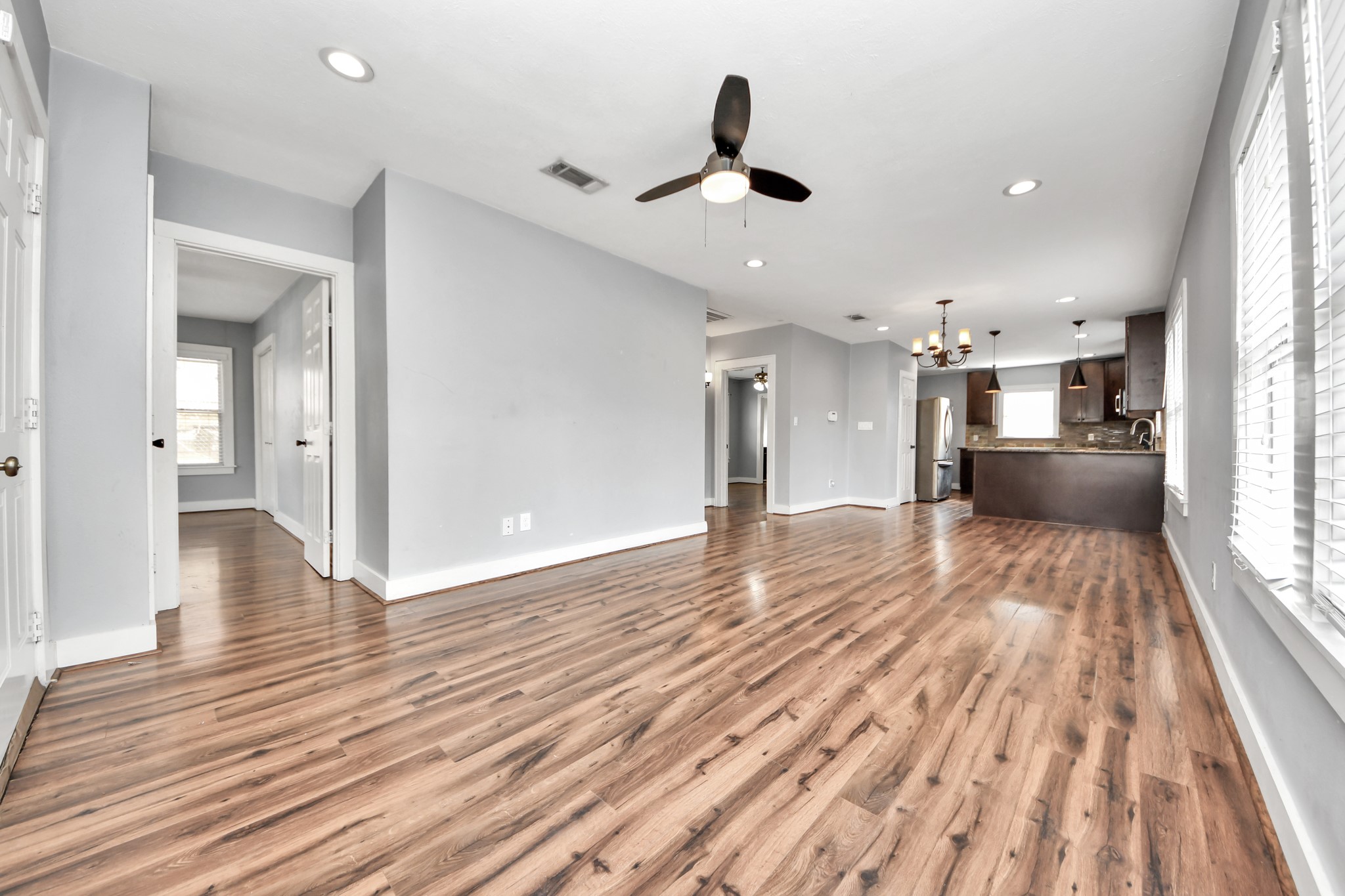 2820 Holman Street Houston, TX 77004 - Photo 12 of 38 This photo showcases a spacious, open-concept living area with attractive wood flooring. The room is well-lit with recessed lighting and natural light from large windows. A ceiling fan is centrally located, and the space flows seamlessly into a modern kitchen with dark cabinetry and stylish light fixtures.