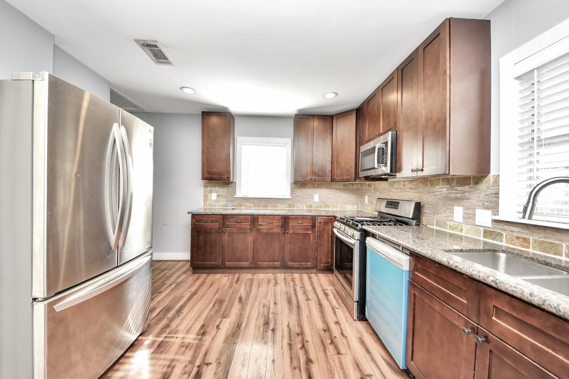2820 Holman Street Houston, TX 77004 - Photo 17 of 38 a kitchen with stainless steel appliances granite countertop a refrigerator a sink dishwasher a stove with wooden cabinets and floor