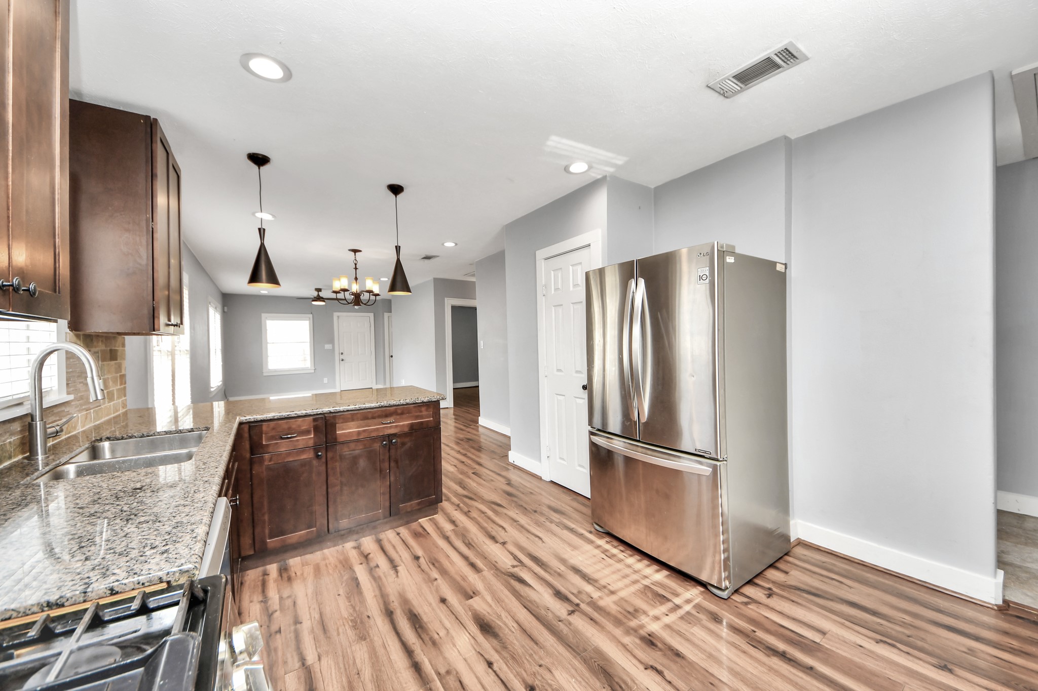 2820 Holman Street Houston, TX 77004 - Photo 20 of 38 This photo showcases a modern kitchen with stainless steel appliances, granite countertops, and dark wood cabinets. The space is well-lit with recessed lighting and pendant lights over the island, complemented by wood flooring throughout.
