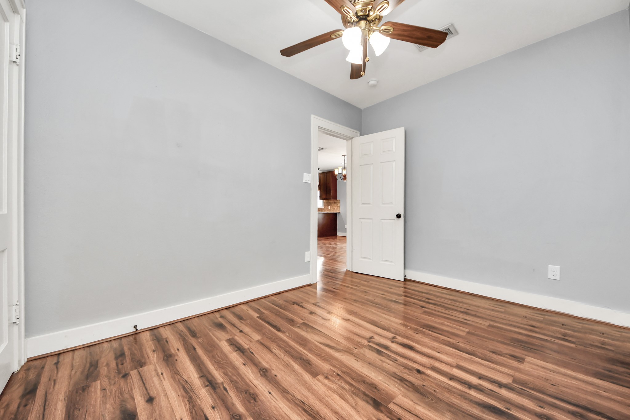 2820 Holman Street Houston, TX 77004 - Photo 23 of 38 This room features sleek hardwood floors, light gray walls, and a ceiling fan with lights. The space is bright and opens to a view of the adjacent kitchen area through a white door.