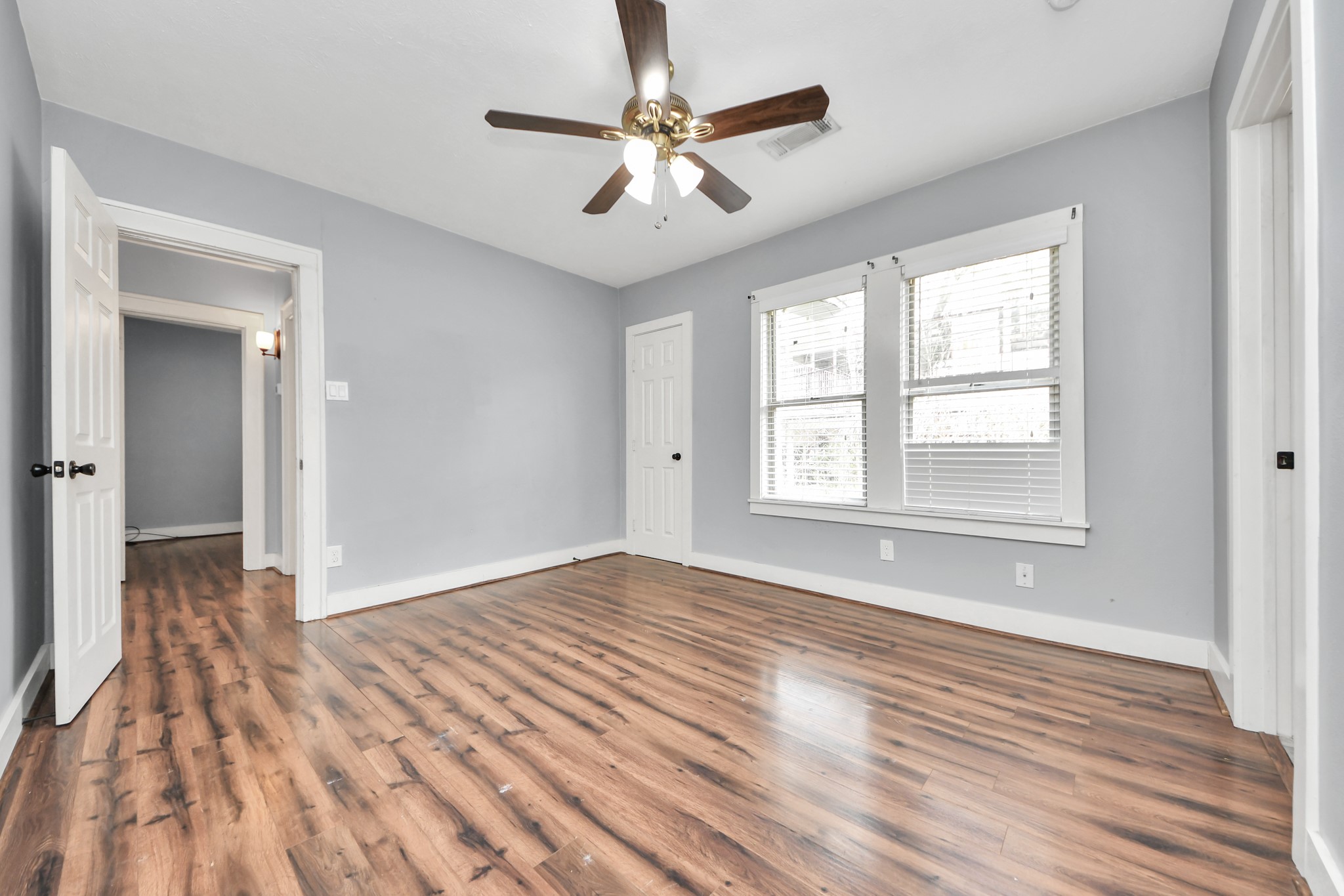 2820 Holman Street Houston, TX 77004 - Photo 26 of 38 Bright bedroom with wood flooring, neutral gray walls, and a ceiling fan. It features large windows for natural light and connects to other rooms via open doorways.