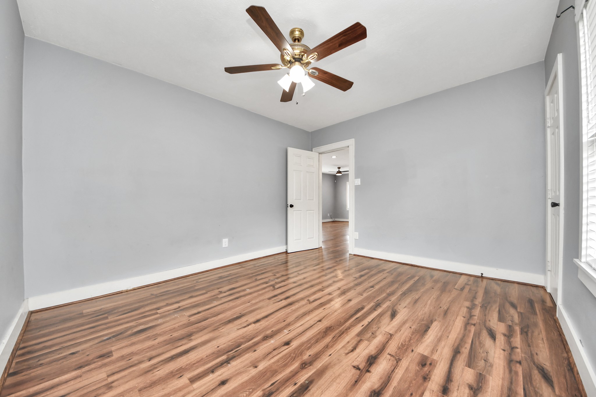 2820 Holman Street Houston, TX 77004 - Photo 27 of 38 This room features hardwood flooring, light gray walls, a ceiling fan, and ample natural light from a window. An open door leads to an adjacent room, enhancing the sense of space.