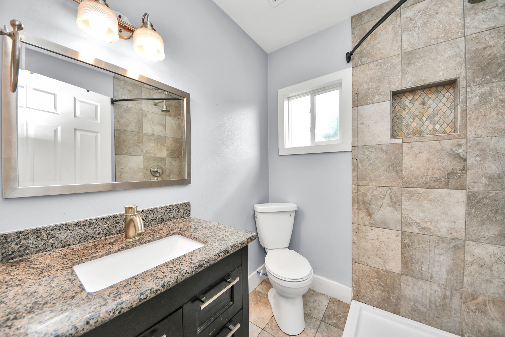2820 Holman Street Houston, TX 77004 - Photo 28 of 38 This modern bathroom features a granite countertop with an undermount sink, a large mirror with stylish lighting, and a tiled shower area with a niche. The neutral tones and clean lines create a fresh, inviting space.