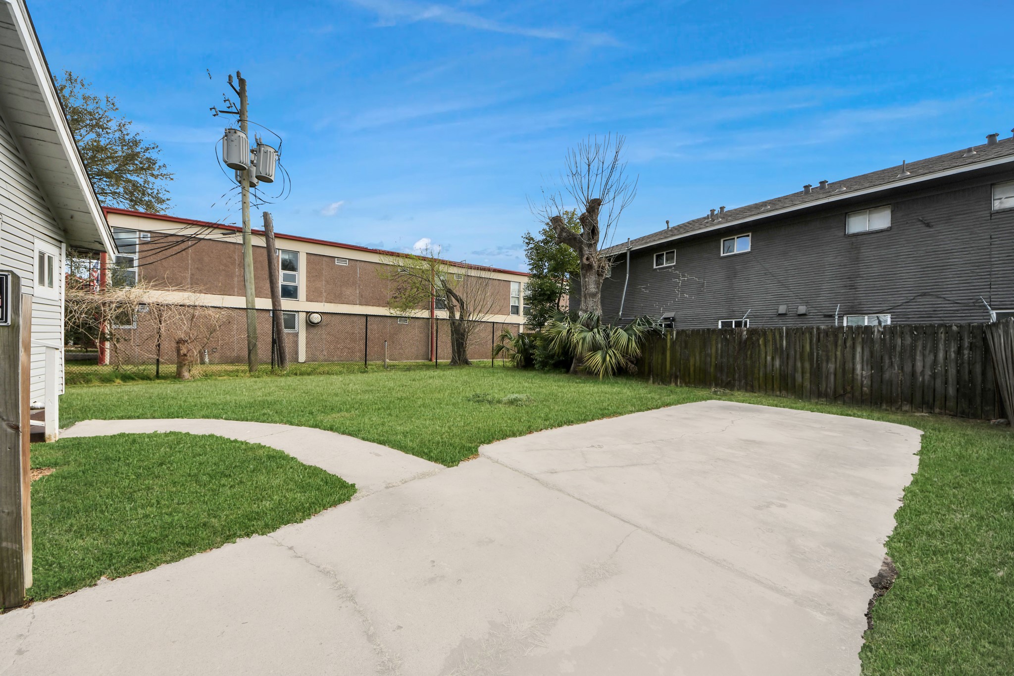 2820 Holman Street Houston, TX 77004 - Photo 34 of 38 Spacious backyard with a concrete driveway and grassy area, bordered by a wooden fence. Nearby utility poles and neighboring buildings are visible, providing a suburban feel.