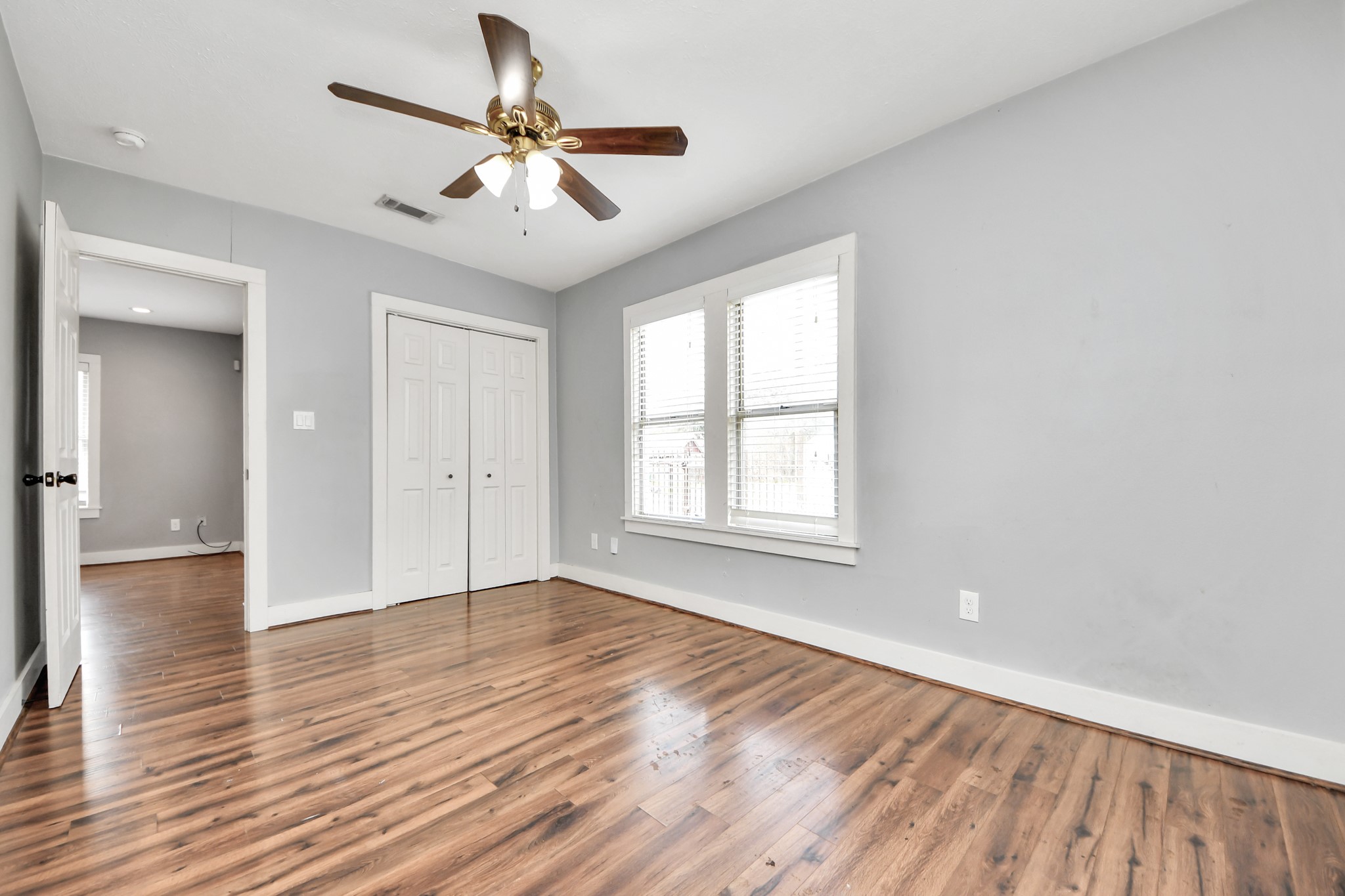 2820 Holman Street Houston, TX 77004 - Photo 4 of 38 The first bedroom is right off the front entry way featuring laminate wood flooring, a ceiling fan, and ample natural light from two large windows. It includes a double-door closet and has a neutral gray color scheme, making it versatile for any decor.