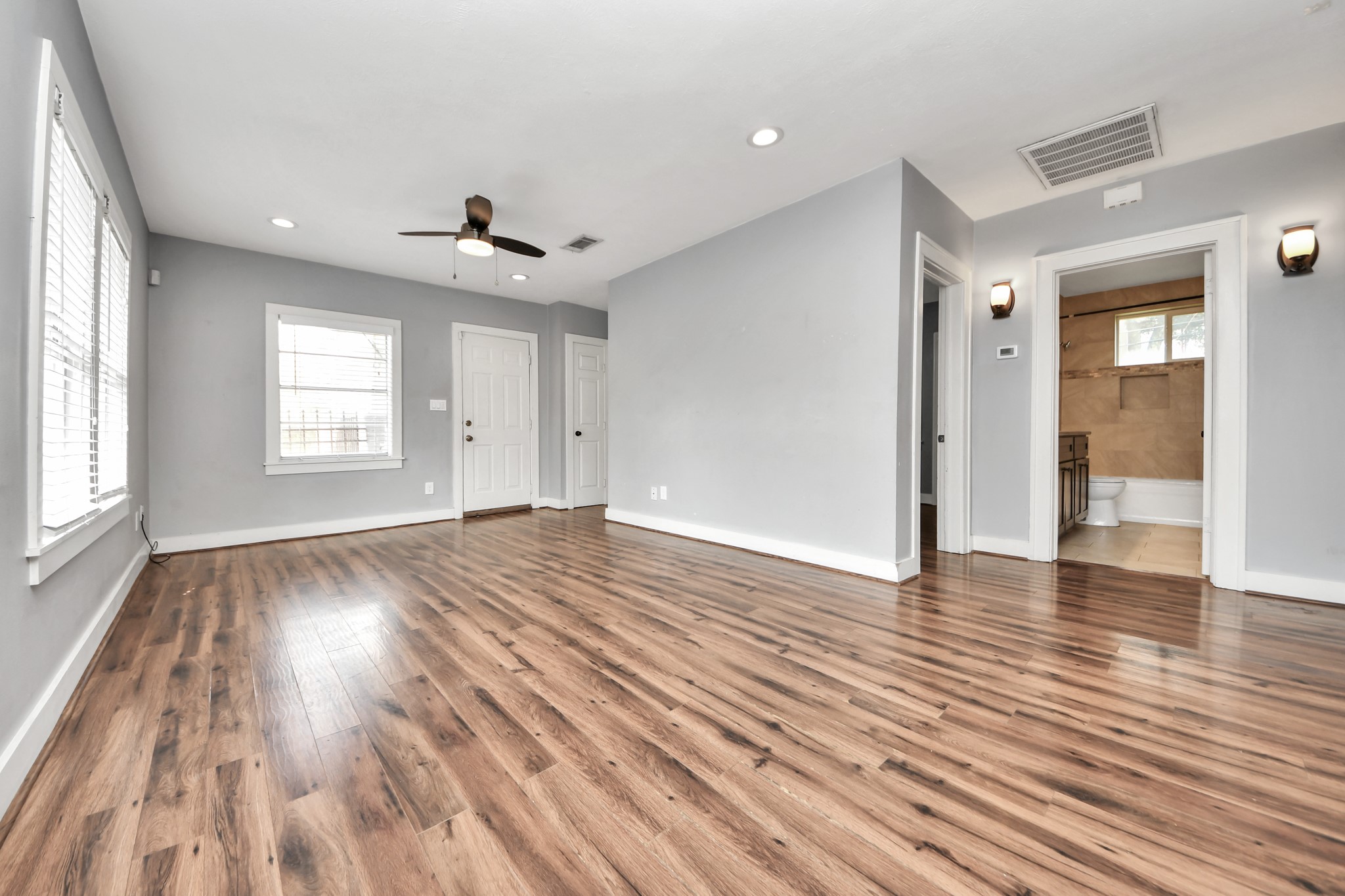 2820 Holman Street Houston, TX 77004 - Photo 8 of 38 Spacious, bright living room with wood laminate flooring, neutral gray walls, and recessed lighting. Features a ceiling fan and multiple windows for natural light. Includes access to a bathroom with modern fixtures.