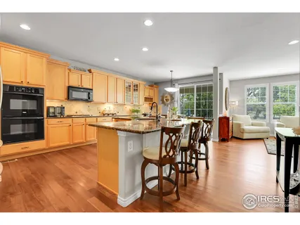 a open kitchen with stainless steel appliances granite countertop a stove top oven a sink a dining table and chairs with wooden floor
