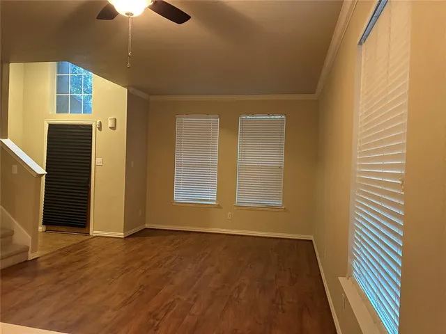 an empty room with wooden floor chandelier fan and windows
