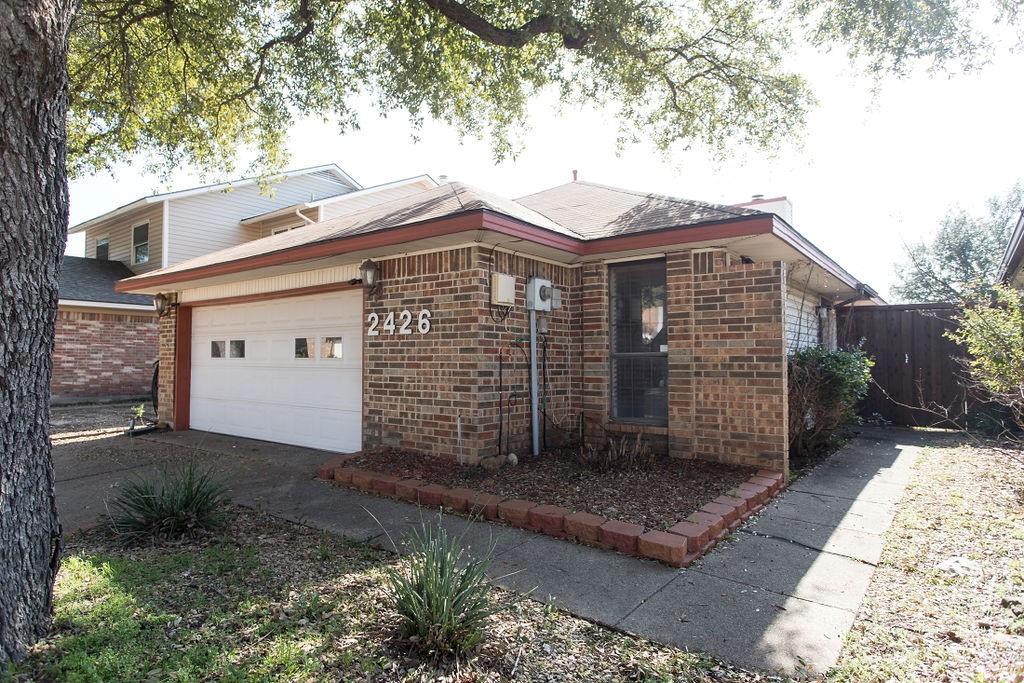 View of front of house featuring dirt driveway, brick siding, fence, and a garage