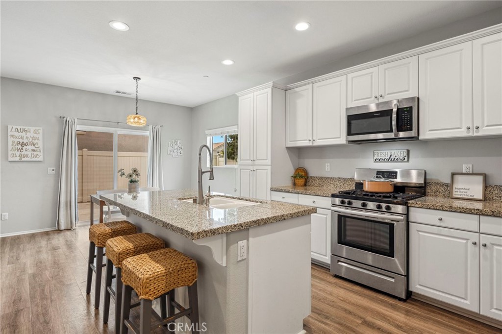 205 Spotted Saddle Way Fallbrook, CA 92028 - Photo 16 of 63 a kitchen with stainless steel appliances granite countertop a stove top oven a sink dishwasher a dining table and chairs with wooden floor