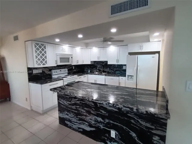 a kitchen with stainless steel appliances granite countertop a refrigerator a sink and white cabinets