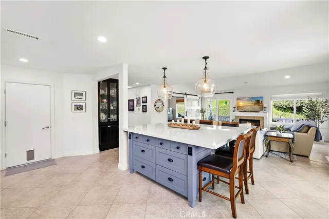 a room with stainless steel appliances kitchen island granite countertop a dining table chairs and a refrigerator