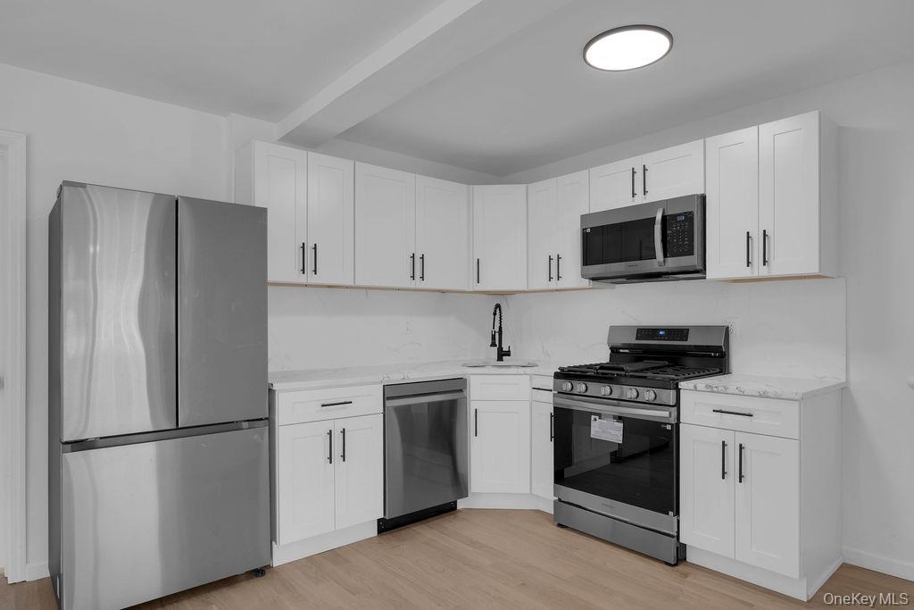 173-62 103rd Road Queens, NY 11433 - Photo 4 of 23 a kitchen with stainless steel appliances white cabinets white stove a microwave and a refrigerator