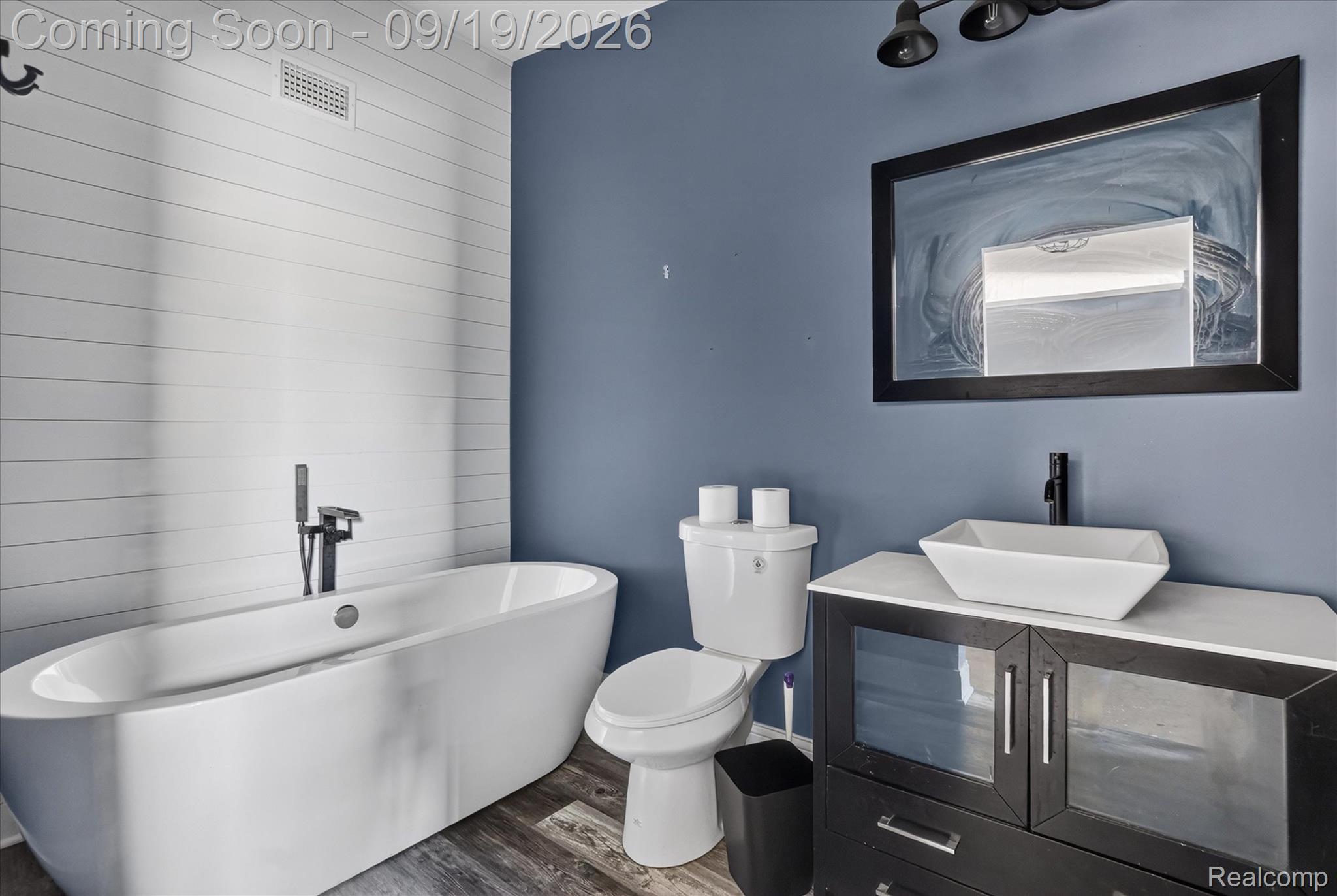 10215 West Mount Morris Road Flushing, MI 48433 - Photo 37 of 58 Freestanding soaking tub with a floor-mounted faucet, wood-finish flooring, white shiplap accent wall, and a vanity with a vessel sink