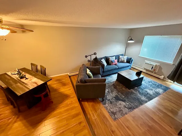 a living room with couches and kitchen view with wooden floor