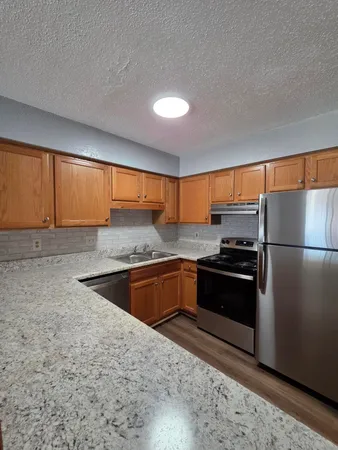 a kitchen with stainless steel appliances granite countertop a refrigerator a sink dishwasher a stove and white wooden cabinets