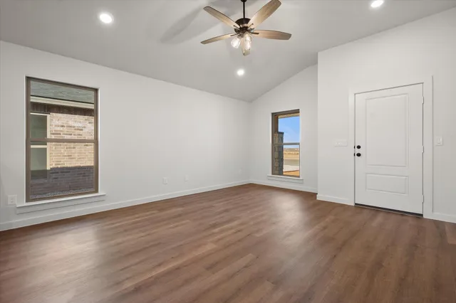 an empty room with wooden floor chandelier fan and windows