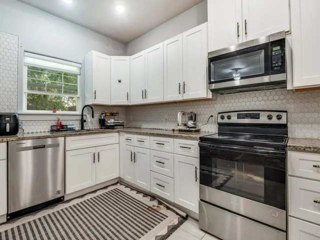 a kitchen with granite countertop white cabinets stainless steel appliances and a window