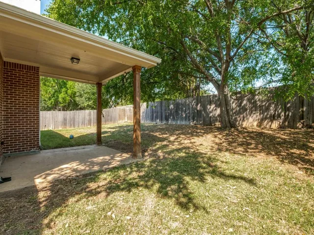 a backyard of a house with large trees and wooden fence