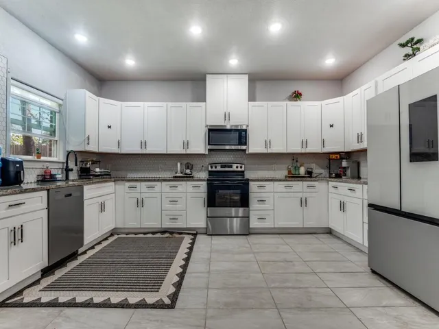 a kitchen with granite countertop a stove top oven a sink dishwasher and a refrigerator with white cabinets