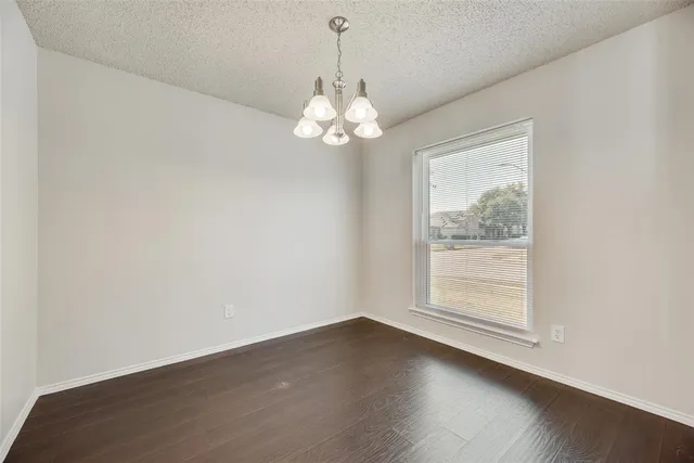 an empty room with wooden floor chandelier and window
