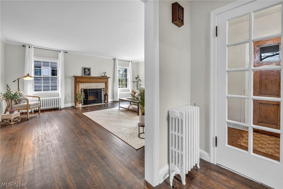 17409 Fernway Road Cleveland, OH 44120 - Photo 5 of 47 Unfurnished living room with a tile fireplace, crown molding, radiator heating unit, and dark wood-type flooring