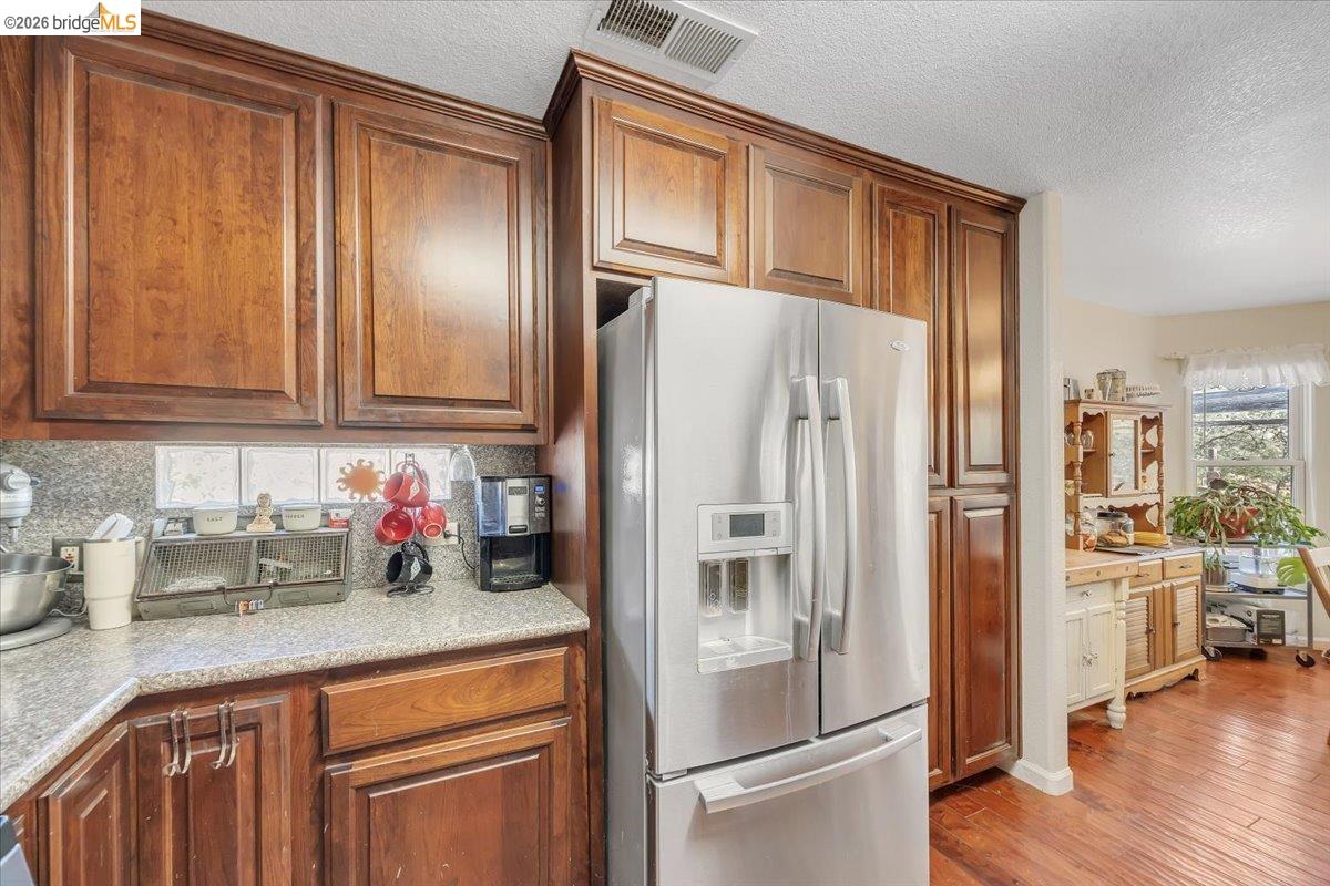 14450 Jacksonville Road Jamestown, CA 95327 - Photo 22 of 85 Warm wood cabinetry, integrated stainless-steel refrigerator, speckled countertop, and wood-finish flooring