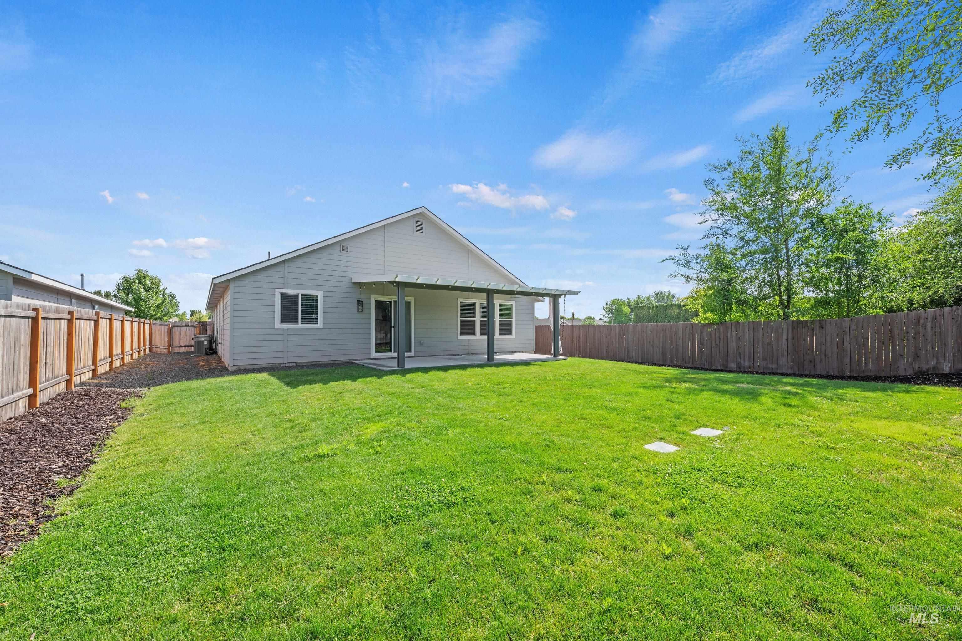 12744 West Fig Street Boise, ID 83713 - Photo 31 of 34 Expansive backyard featuring a lush green lawn, mature perimeter trees, and a covered concrete patio