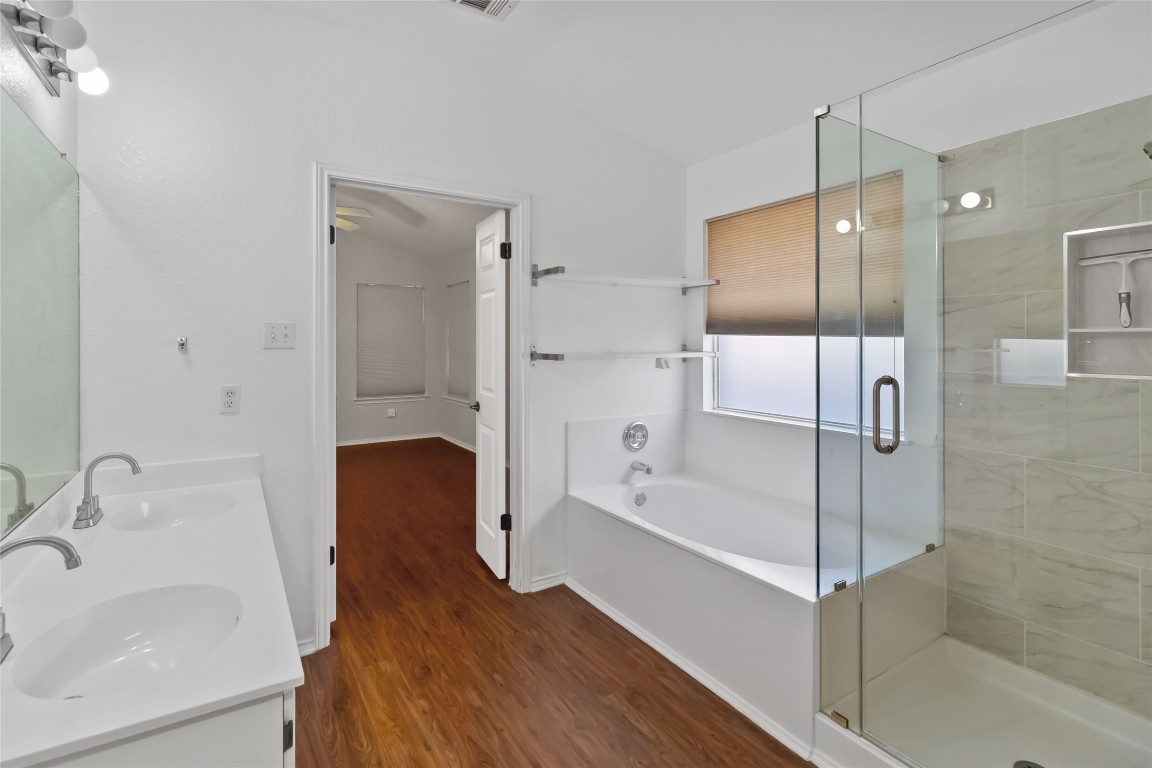 1320 Lochaline Loop Pflugerville, TX 78660 - Photo 19 of 35 Bathroom featuring a garden tub, double vanity, a stall shower, vaulted ceiling, and dark wood-style flooring